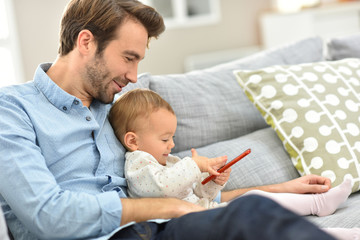 Obraz premium Daddy and baby girl playing with smartphone
