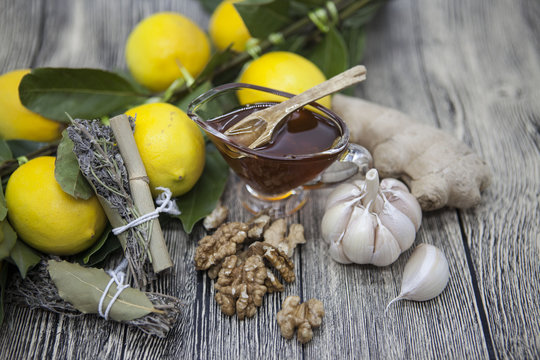 The composition of glass vase with floral honey and wooden spoon with lemon provencal herbs walnuts, garlic  and ginger on a wooden background