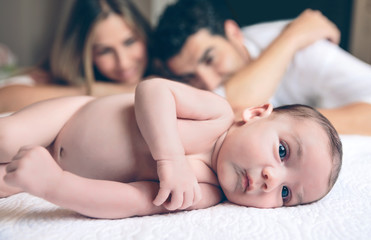 Newborn lying over bed and couple smiling on background