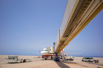 Passagierflugzeug verbunden mit einem Fluggaststeig, umgeben von Servicefahrzeugen - Weitwinkel 