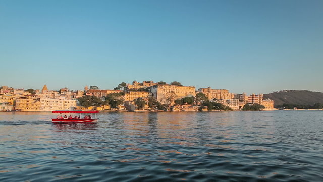 Tourist boat passing in front of Udaipur City Palace, view  from Lake Pichola on sunset. Udaipur, India