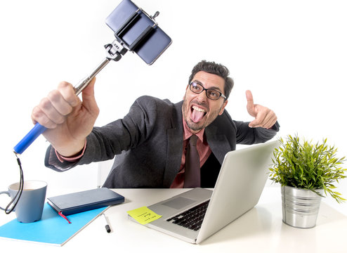 funny businessman at office desk taking selfie photo with mobile phone camera and stick