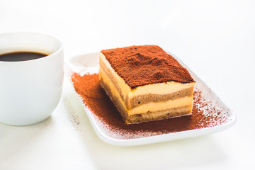 Tasty tiramisu cake with coffee cup on white background