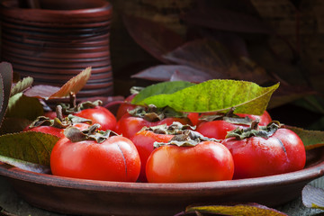 Ripe persimmons with leaves on a clay plate in a rustic style, s