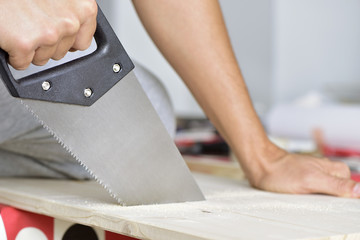 young man sawing a wooden board with a handsaw