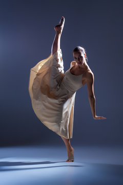 Young beautiful dancer in beige dress dancing on gray background