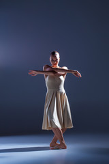 Obraz premium Young beautiful dancer in beige dress dancing on gray background