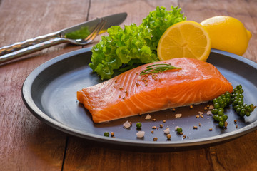 Fresh salmon with lemon on black dish.