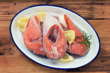frozen salmon with lemon on white dish on brown wooden background
