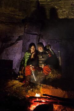 Medieval King in armor with jugger is sitting on furs near the c