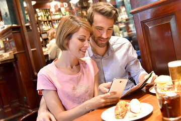 Couple of tourists in restaurant looking at map and smartphone