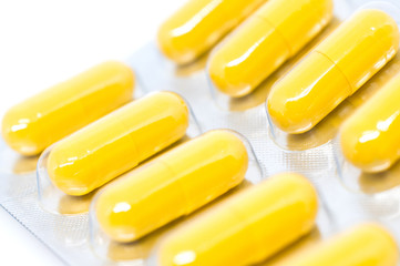 yellow pills in blister pack closeup selective focus white backg