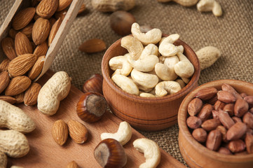 Almonds, cashew and hazelnuts in wooden bowls on wooden and burlap