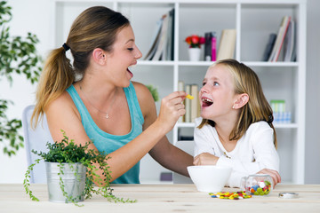 Young mother and daughter eating sweets at home.