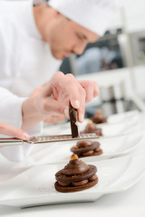 close up of professional pastry cook hands preparing chocolate dessert in restaurant kitchen