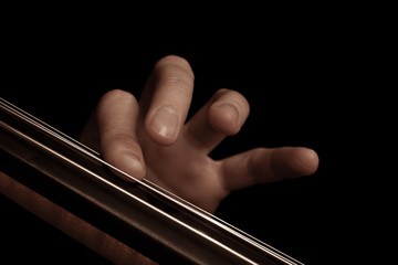 The fingers on the strings of the cello on a black background 