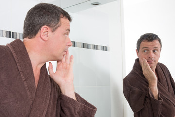 Handsome man in front of mirror applying cosmetics