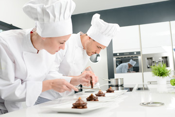 pastry cook professional team man and woman in restaurant kitchen preparing a chocolate dessert - obrazy, fototapety, plakaty