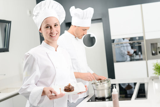 portrait of a cheerful young woman professional pastry cook at work in kitchen decorating a chocolate dessert