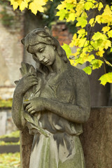 Fototapeta na wymiar Stone Girl on Tomb from autumn mystery old Prague Cemetery, Czech Republic