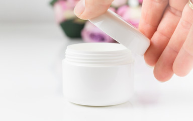 Die rechte Hand einer Frau &ouml;ffnet eine wei&szlig;e Cremedose.