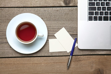 Blank business cards with pen, laptop and tea cup on wooden office table