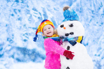 Little girl building a snow man in winter