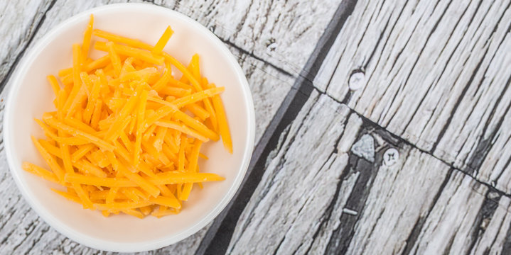 Grated cheddar cheese in white bowl over wooden background