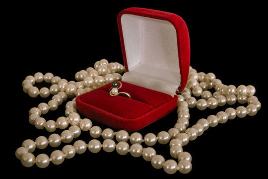 Ring in a box. Ring in the red box and a pearl necklace on a black background.