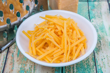 Grated cheddar cheese with steel grater over wooden background