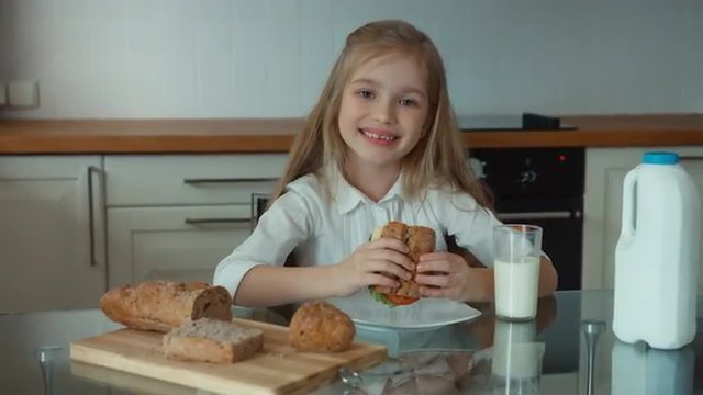 Girl eating a sandwich and smiling at camera. Child sitting at the kitchen table