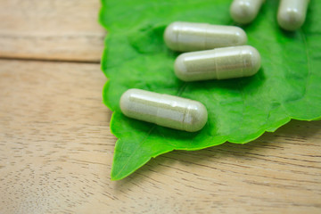 herbal medicine capsules with green herb leaf on wood table