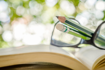Close up of pencil , eyeglasses and open book on bokeh backgroun
