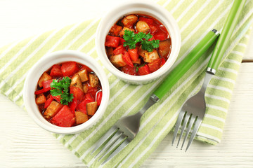 Tasty vegetarian ratatouille made of eggplants, squash, tomatoes in bowls on wooden table background