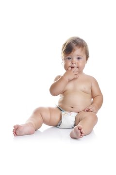 Adorable baby boy sitting with fingers in his mouth on a white background