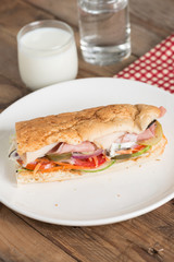 Long sandwich with chicken ham and pork ham on white plate.