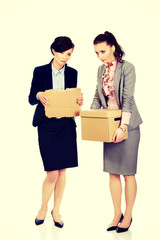 Two sad businesswoman carrying box.