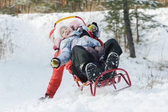 Excited sibling children laughing during sledding down snowy hill by wooden sled