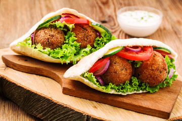 Falafel and fresh vegetables in pita bread on wooden table