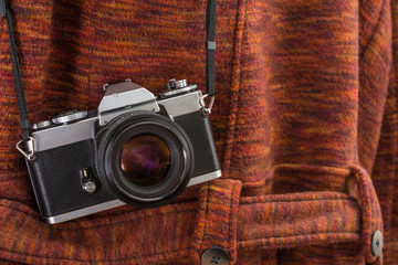 A vintage camera hanging on a strap over a red coats shoulder