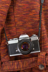 A vintage camera hanging on a strap over a red coats shoulder