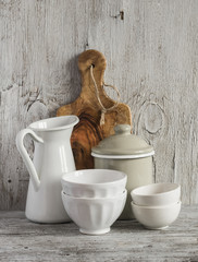 vintage crockery - enamel jug, enameled jar, white ceramic bowl and olive cutting board on a light wooden background