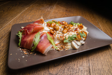 Decorate tagliatelle with cheese sauce, mushrooms and chicken. On top of this dish is arugula, prosciutto, ham and almonds. Everything is served on a plate and it is ready for consummation.