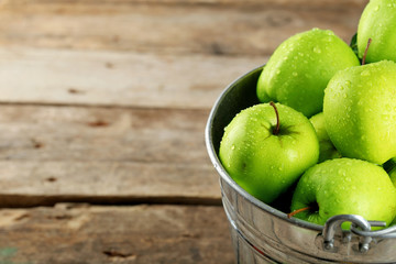 Ripe green apple in metal bucket on wooden table close up