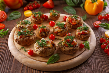 A wooden tablet with stuffed mushrooms and vegetables on the table