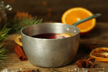 Mulled wine in stew-pan on decorated wooden background