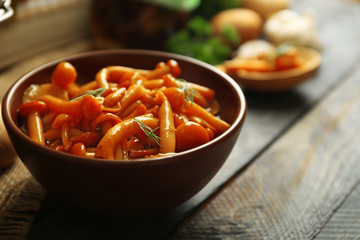 Delicious marinated mushrooms in bowl on wooden background