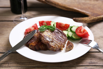 Roasted beef fillet and fresh vegetables on plate, on wooden background