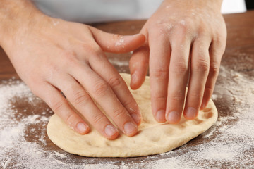 Hands preparing dough basis for pizza on the wooden table, close-up