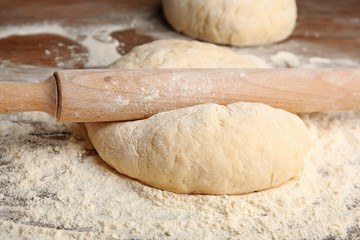 Dough for pizza and rolling-pin on wooden table